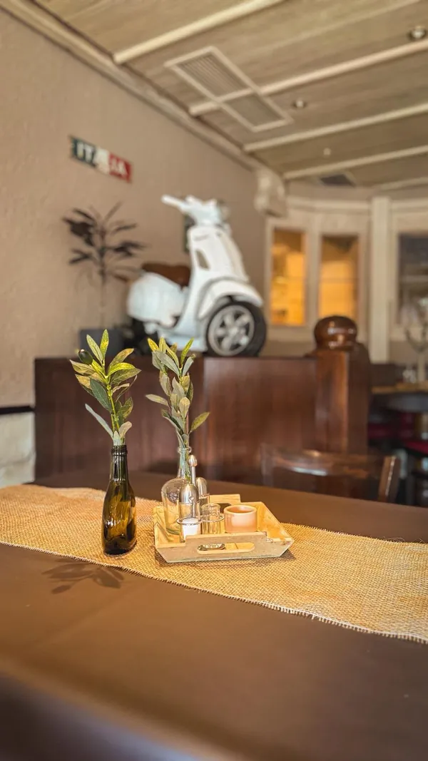 Gedeckter Tisch mit Olivenzweig, im Hintergrund eine weiße Vespa